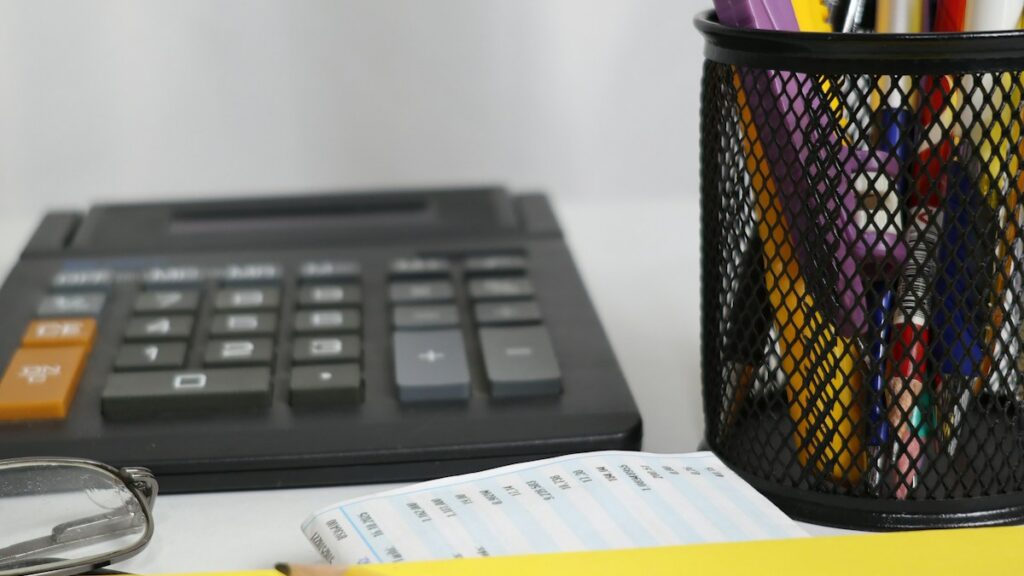 Calculator, pens and envelope on a desk, illustrating a recurring-expense review